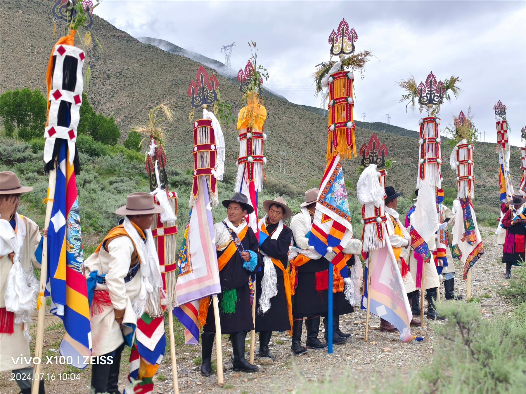 Villagers in traditional dress carrying tall ceremonial banners through the fields