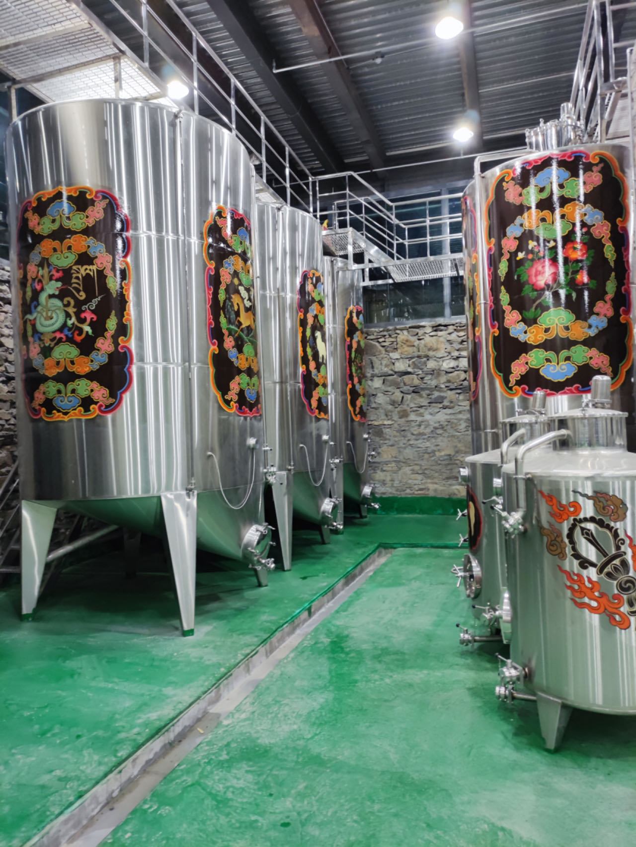 Stainless steel fermentation tanks, each painted with a Tibetan medallion